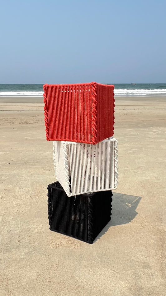 HOUSE OF STRINGS Embrace cube pendant lamps in red, white, and black cotton cord stacked on a sandy beach.